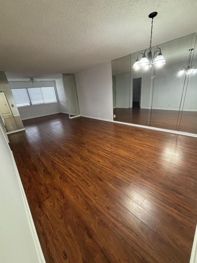 unfurnished dining area featuring dark hardwood / wood-style flooring, ceiling fan with notable chandelier, and a textured ceiling