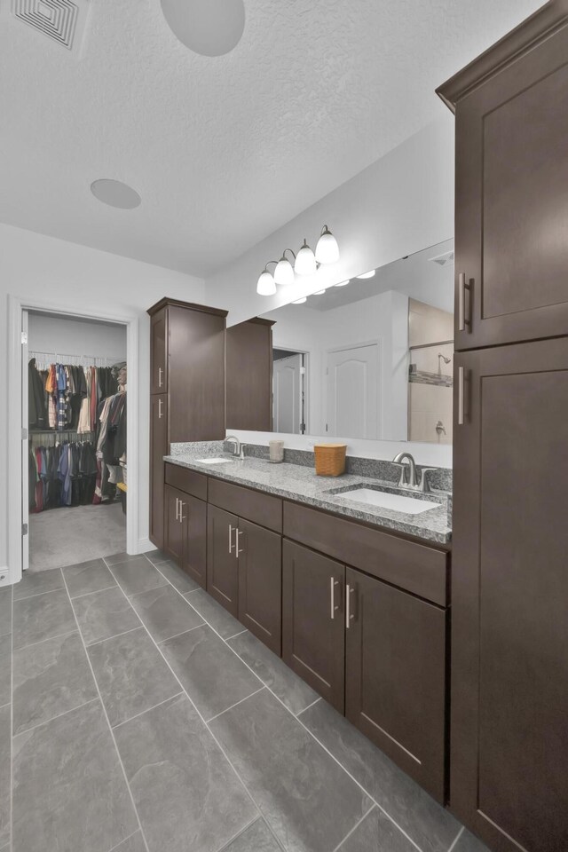 1316 SW Abacus Ave, Port Saint Lucie, FL 34953 - bathroom featuring double vanity, a textured ceiling, a spacious closet, and a shower