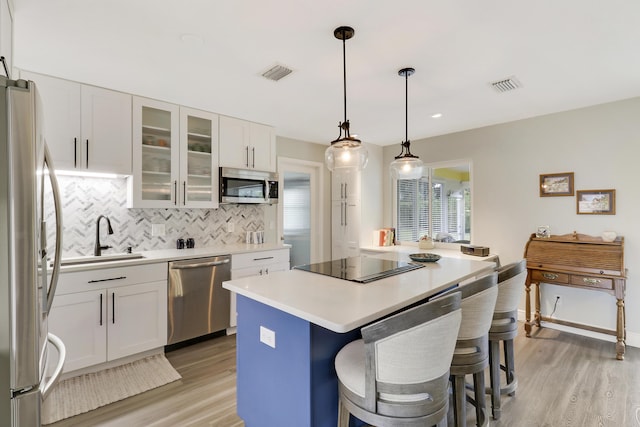 kitchen with a kitchen island, sink, white cabinets, hanging light fixtures, and stainless steel appliances