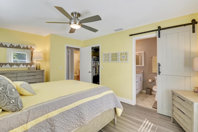 bedroom featuring ensuite bathroom, a spacious closet, ceiling fan, a barn door, and a closet