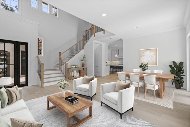 living room with ornamental molding, a high ceiling, and light wood-type flooring