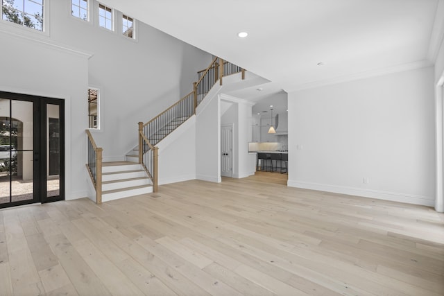 unfurnished living room with crown molding, light hardwood / wood-style flooring, and a towering ceiling