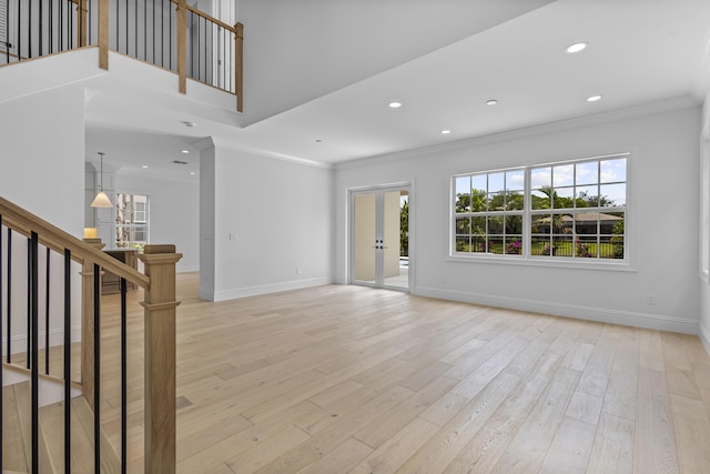 unfurnished living room with crown molding, light wood-type flooring, french doors, and a wealth of natural light