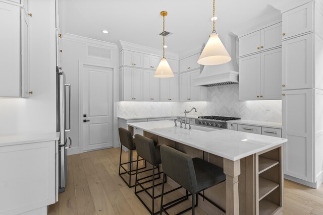 kitchen featuring pendant lighting, an island with sink, a breakfast bar area, white cabinets, and light stone counters