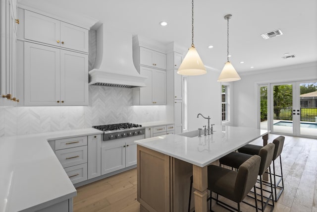 kitchen with sink, custom exhaust hood, stainless steel gas stovetop, and a center island with sink