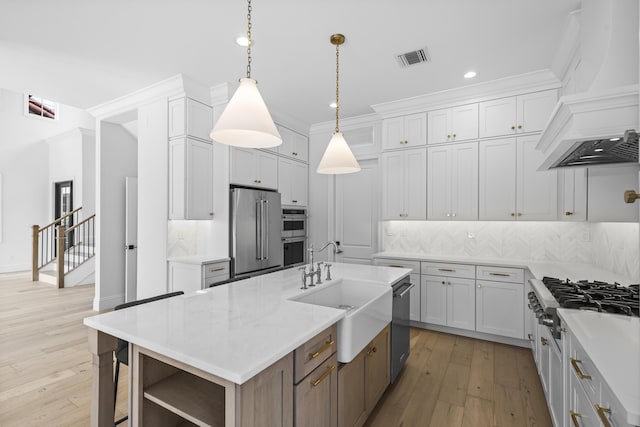 kitchen with an island with sink, appliances with stainless steel finishes, custom range hood, and white cabinets