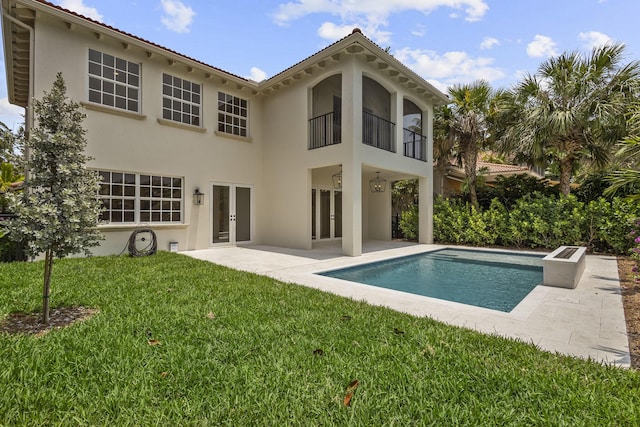 rear view of property featuring a lawn, a patio, and a balcony