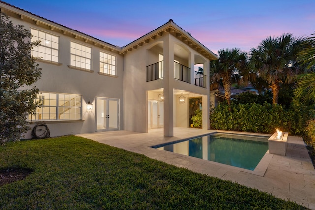 back house at dusk featuring a lawn, a patio, a balcony, and an outdoor fire pit