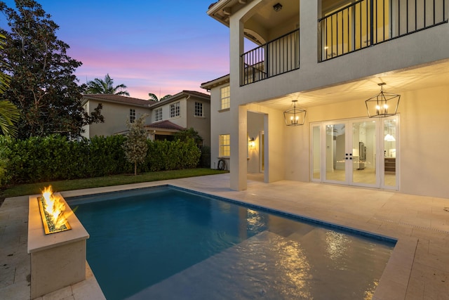 pool at dusk with french doors, an outdoor fire pit, and a patio