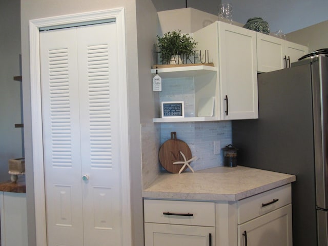 kitchen featuring stainless steel refrigerator, decorative backsplash, and white cabinets