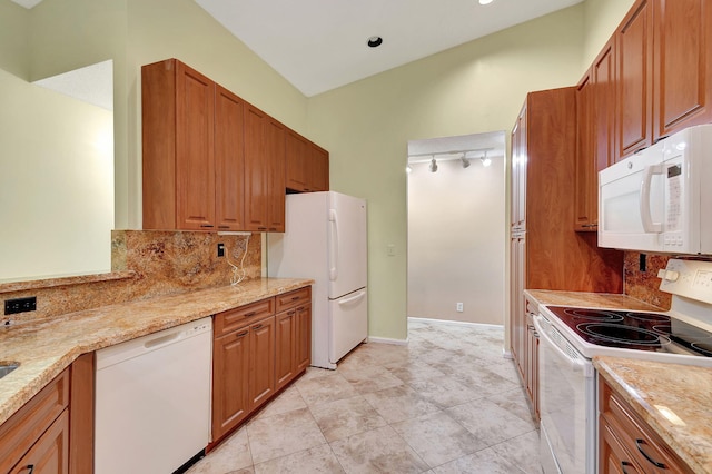 kitchen with light stone counters, white appliances, rail lighting, and backsplash