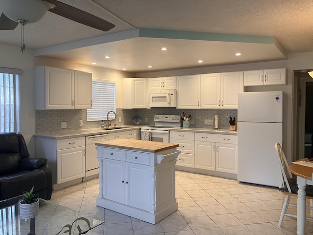 kitchen with light tile patterned flooring, a kitchen island, white cabinetry, sink, and white appliances