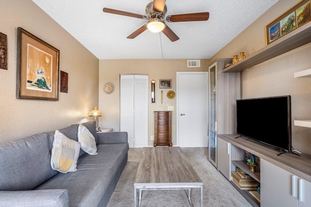 living room featuring ceiling fan, light carpet, and a textured ceiling