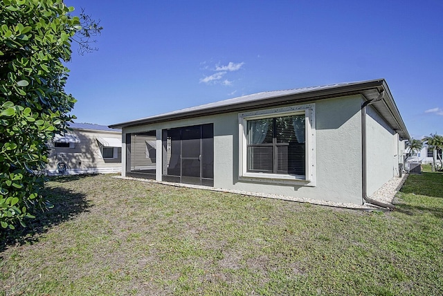 rear view of house featuring a sunroom, a lawn, and stucco siding