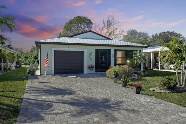 view of front of house featuring a lawn, metal roof, an attached garage, decorative driveway, and stucco siding