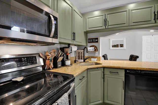 kitchen with sink, appliances with stainless steel finishes, light stone counters, green cabinetry, and kitchen peninsula