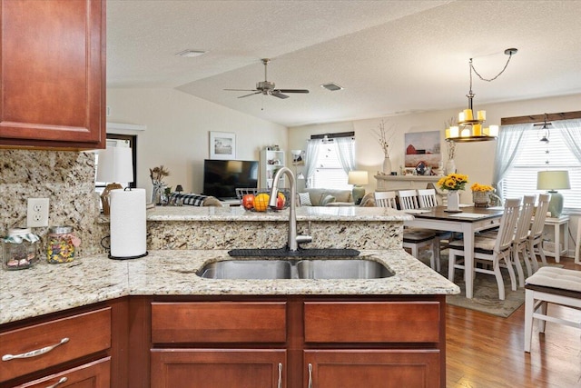 kitchen featuring lofted ceiling, sink, backsplash, ceiling fan, and light stone counters