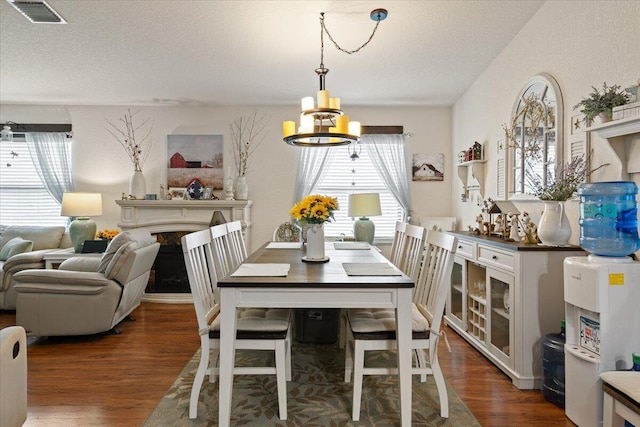 dining room with dark hardwood / wood-style flooring, a premium fireplace, a textured ceiling, and an inviting chandelier