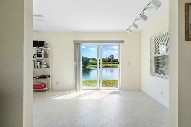 spare room featuring a water view, rail lighting, and light tile patterned floors