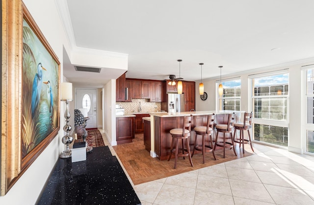 kitchen featuring light tile patterned floors, hanging light fixtures, a kitchen breakfast bar, stainless steel refrigerator with ice dispenser, and ornamental molding