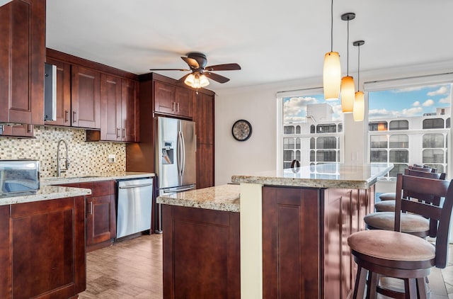 kitchen featuring a kitchen bar, appliances with stainless steel finishes, a kitchen island, light stone countertops, and decorative backsplash