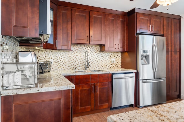 kitchen with light stone counters, stainless steel appliances, sink, and light hardwood / wood-style flooring