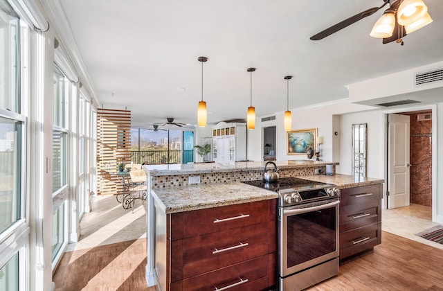 kitchen featuring stainless steel electric range, crown molding, hanging light fixtures, light stone counters, and a large island with sink