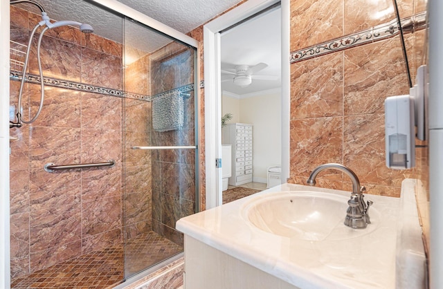 bathroom with a shower with shower door, crown molding, a textured ceiling, vanity, and ceiling fan