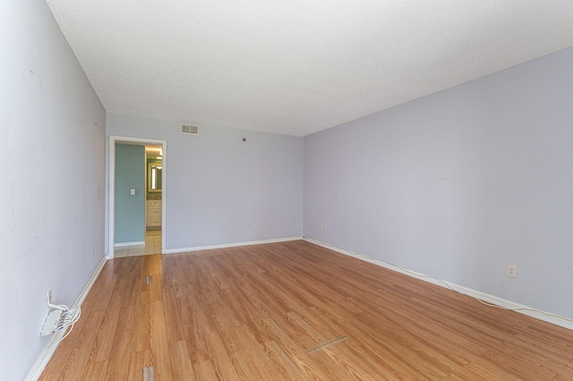 empty room with a textured ceiling and light hardwood / wood-style flooring