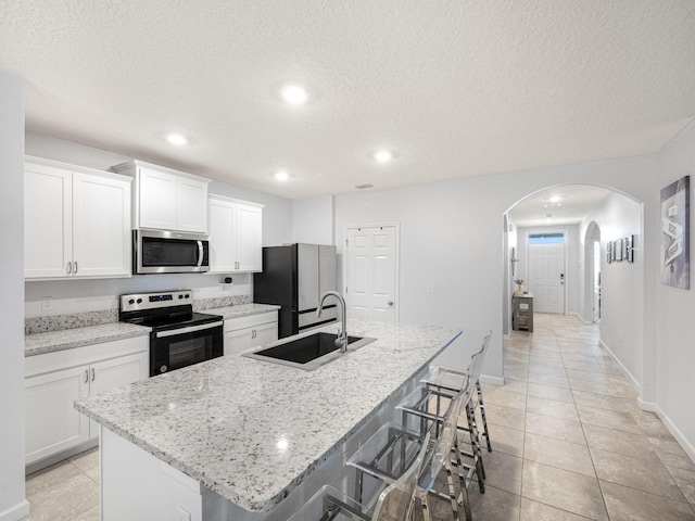 kitchen with white cabinetry, fridge, a kitchen breakfast bar, electric stove, and a kitchen island with sink