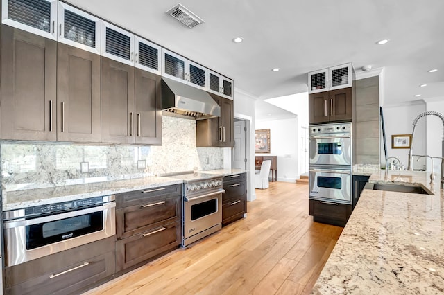 kitchen featuring wall chimney range hood, crown molding, sink, appliances with stainless steel finishes, and light stone counters