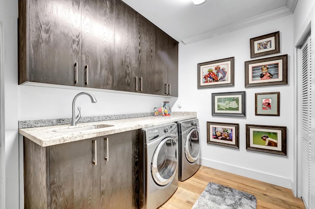 laundry area with sink, cabinets, light hardwood / wood-style floors, ornamental molding, and washing machine and clothes dryer