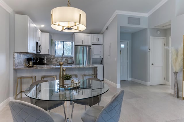 dining space with ornamental molding and stacked washer and clothes dryer