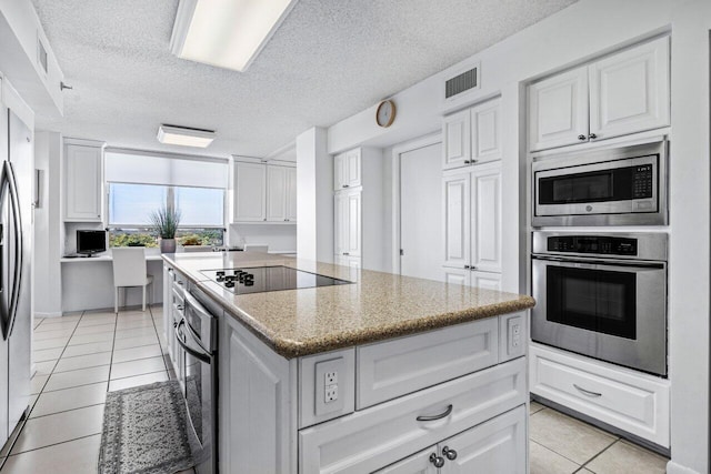 kitchen featuring appliances with stainless steel finishes, white cabinetry, light stone countertops, a kitchen island, and light tile patterned flooring