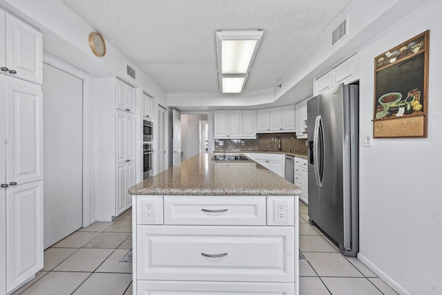 kitchen featuring sink, a center island, light tile patterned floors, stainless steel appliances, and white cabinets