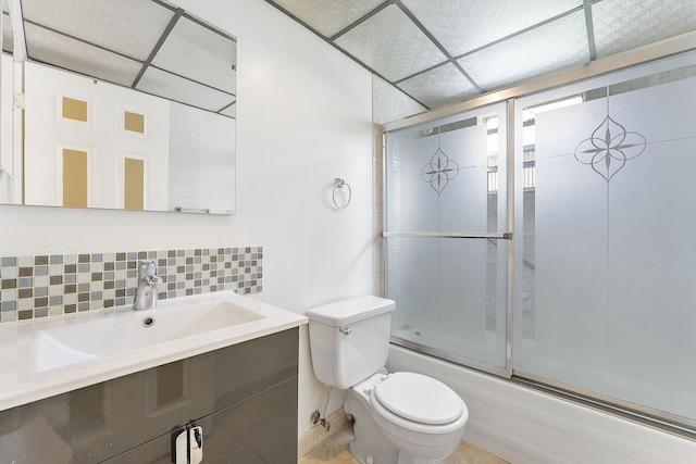 full bathroom with toilet, a paneled ceiling, shower / bath combination with glass door, vanity, and backsplash