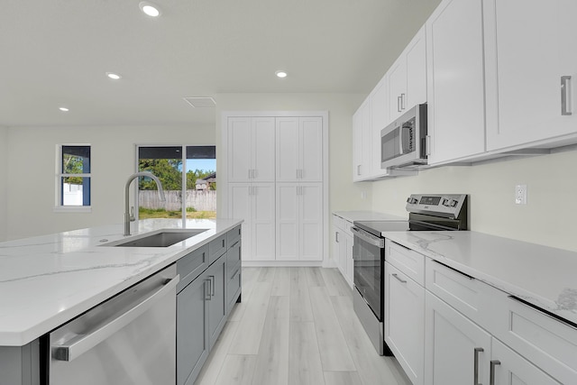 kitchen with sink, white cabinetry, light hardwood / wood-style flooring, stainless steel appliances, and light stone countertops