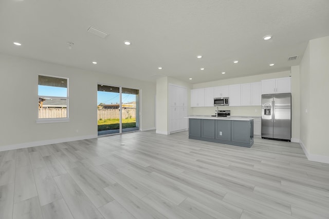 kitchen featuring a kitchen island with sink, white cabinetry, gray cabinetry, stainless steel appliances, and light wood-type flooring