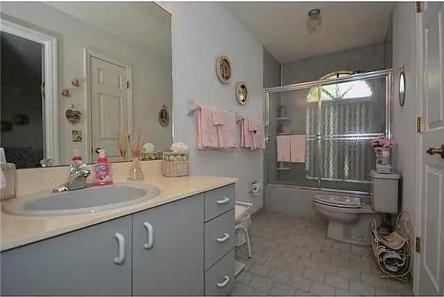 full bathroom with toilet, tile patterned floors, bath / shower combo with glass door, and vanity