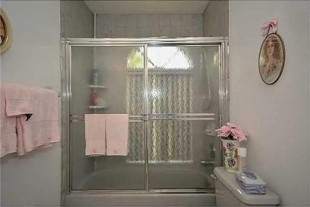 bathroom with toilet and combined bath / shower with glass door