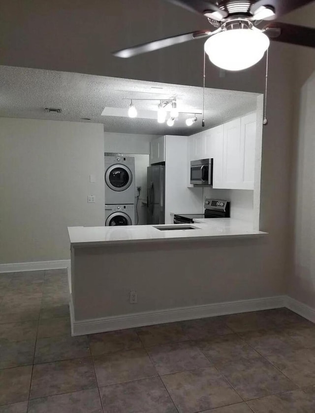 kitchen with stacked washer and dryer, appliances with stainless steel finishes, a textured ceiling, white cabinets, and kitchen peninsula