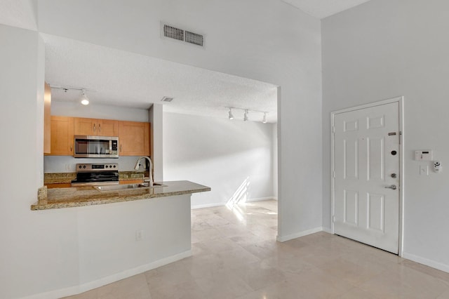 kitchen featuring appliances with stainless steel finishes, light brown cabinetry, sink, kitchen peninsula, and a textured ceiling