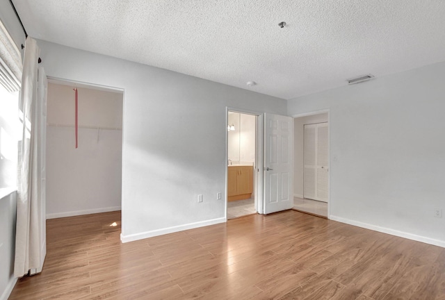 unfurnished bedroom with a spacious closet, light hardwood / wood-style floors, a closet, and a textured ceiling