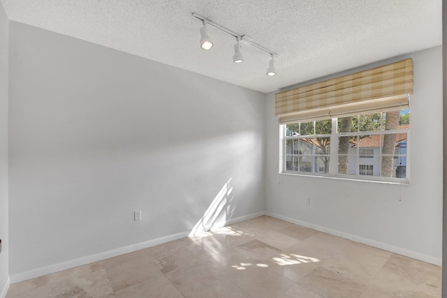 unfurnished room with track lighting and a textured ceiling