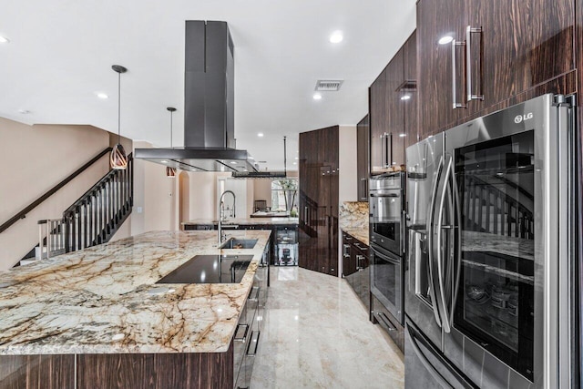 kitchen with appliances with stainless steel finishes, island range hood, a large island with sink, hanging light fixtures, and light stone counters