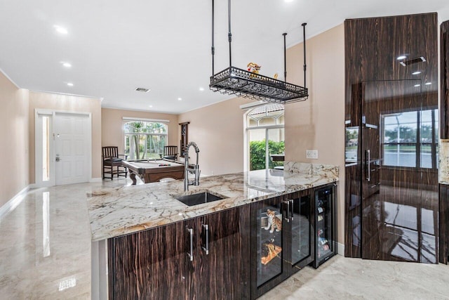 kitchen featuring wine cooler, dark brown cabinetry, light stone countertops, and sink