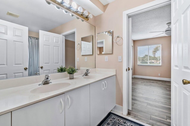 bathroom with hardwood / wood-style flooring, vanity, ceiling fan, and a textured ceiling