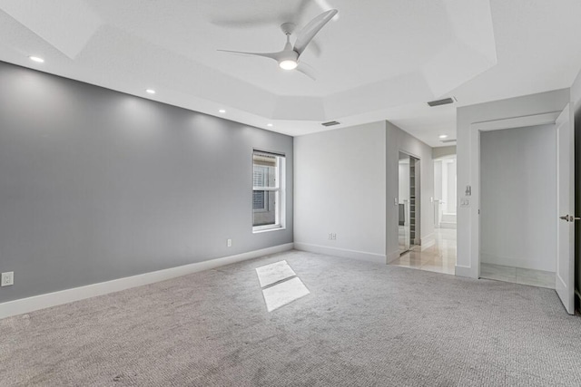 unfurnished room with a raised ceiling, light carpet, and ceiling fan