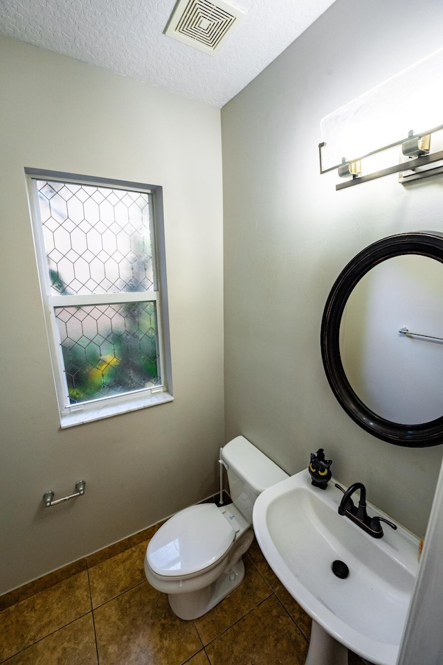bathroom featuring tile patterned floors, visible vents, toilet, a sink, and a textured ceiling