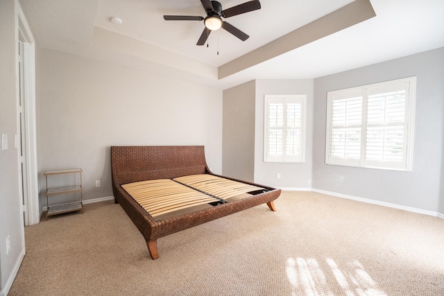 carpeted bedroom with ceiling fan, baseboards, and a tray ceiling